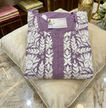 Folded purple garment with white leaf pattern on a beige pillow