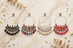 Flat-lay shot of four Chandbali silver hoop earrings arranged on cream marble with gold veining — black onyx, rainbow multi-colour, white pearl, and pink-orange Meenakari styles, accented with gold leaf and botanical sprigs.