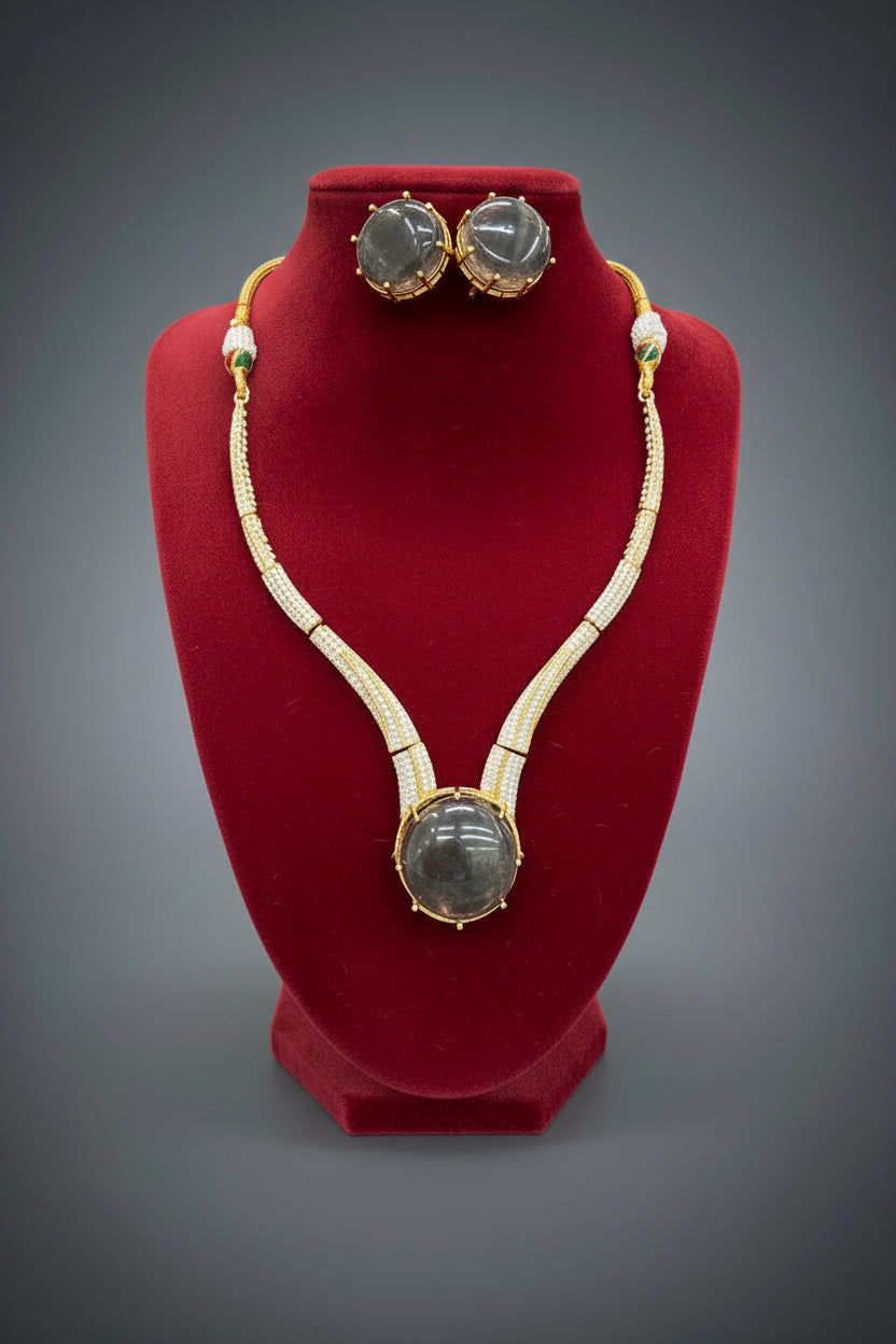 Gold-plated double-strand necklace and matching stud earrings with large round dark grey gemstones, displayed on a black velvet jewellery bust. A hand is holding the display stand.