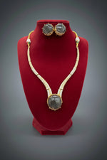 Gold-plated double-strand necklace and matching stud earrings with large round dark grey gemstones, displayed on a black velvet jewellery bust. A hand is holding the display stand.