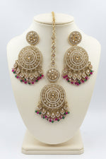 Gold-toned Indian maang tikka with matching stud earrings, decorated with clear crystals and colourful dangling beads in pink, green, yellow, and blue, displayed on a black background with a clear card.
