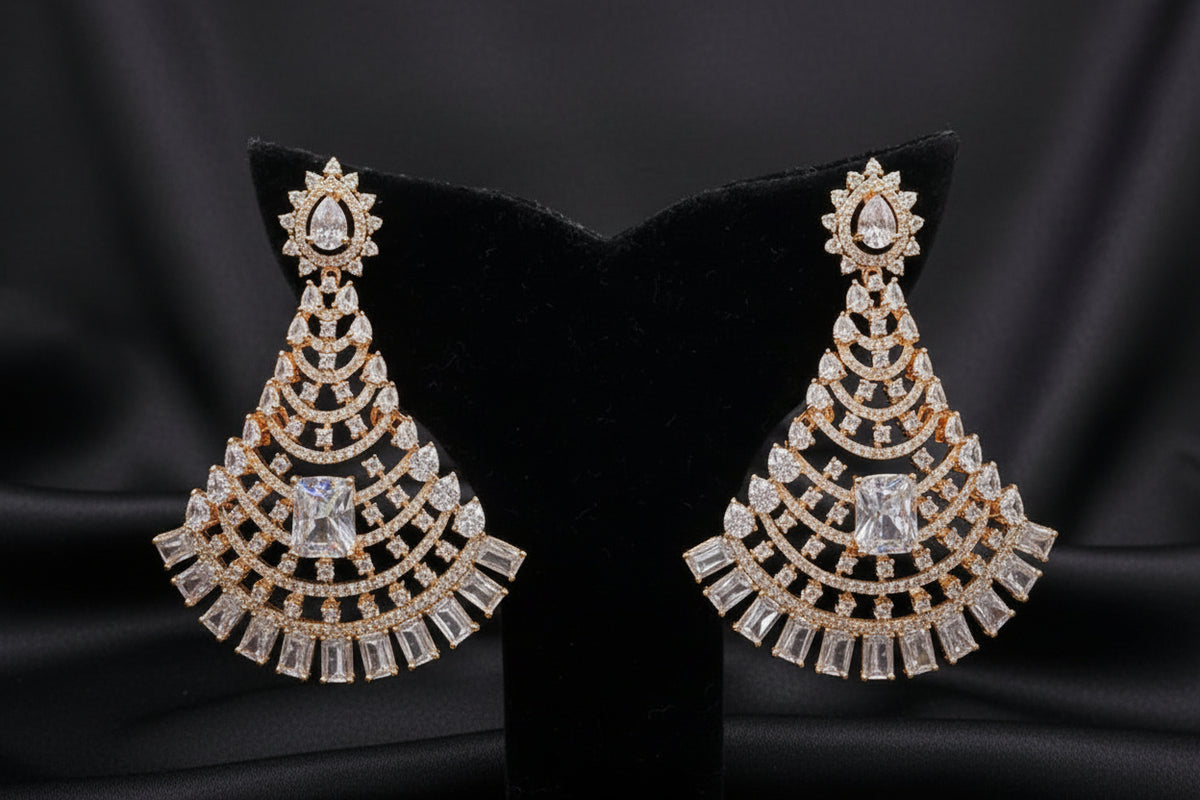 Gold-toned statement earrings displayed on a black velvet jewellery bust, set on a glass display counter with other jewellery visible in the background.