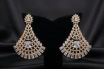 Gold-toned statement earrings displayed on a black velvet jewellery bust, set on a glass display counter with other jewellery visible in the background.
