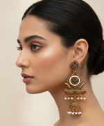 Gold-toned traditional Indian jhumka earrings with white pearl bead borders, green and red stone accents, and dangling pearl beads, displayed on a light marble surface.