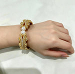 Famaza Couture gold-tone open cuff bracelet featuring two lustrous white pearls at the center, encrusted with hand-set clear pavé crystals in an ornate layered design, worn on a wrist against a soft white background — luxury bridal and formal statement jewellry.