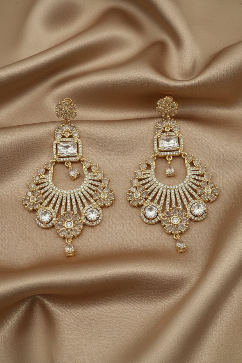 Gold and American diamond stones earrings held by a hand against a neutral background