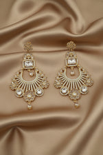 Gold and American diamond stones earrings held by a hand against a neutral background