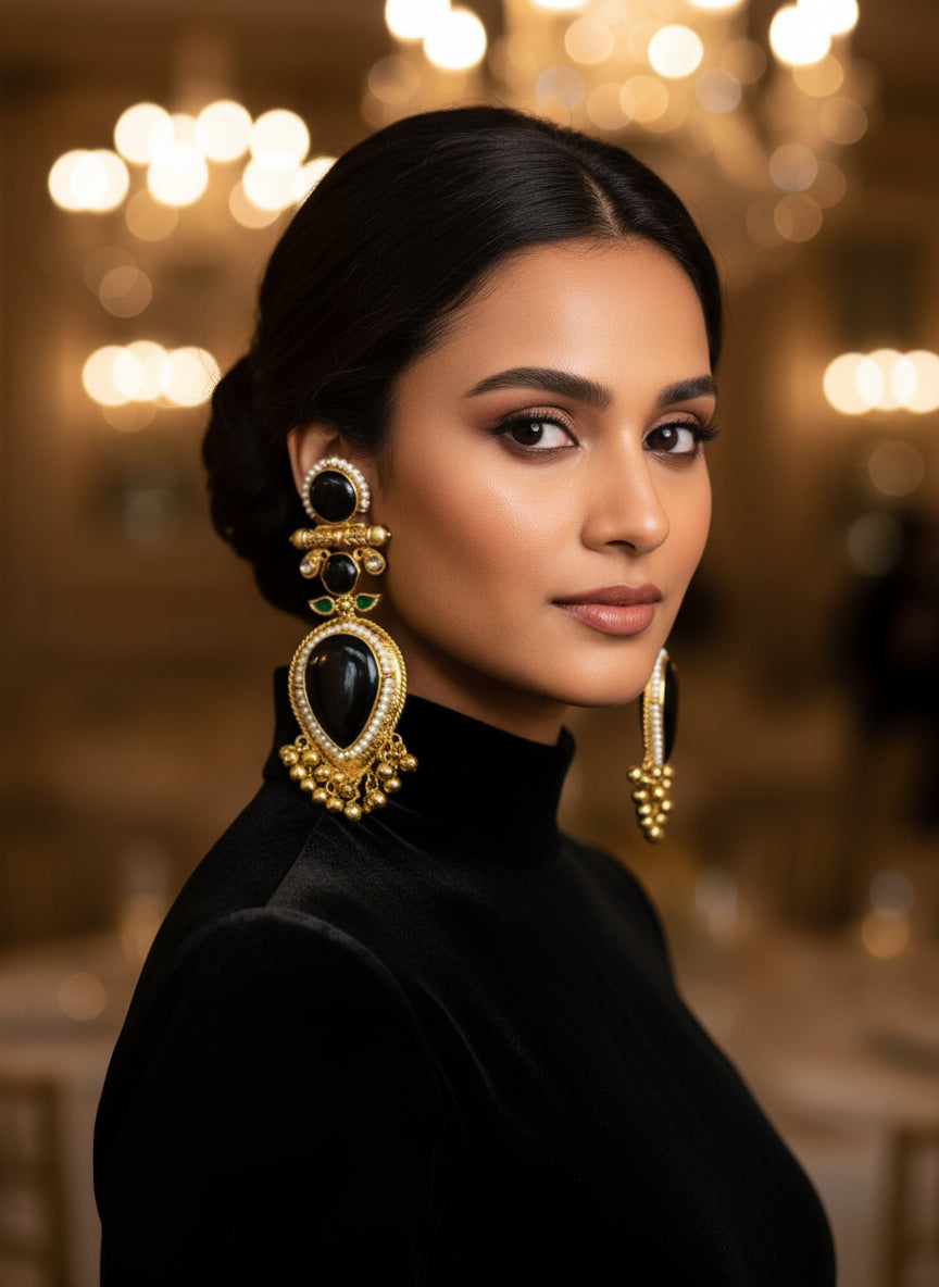 Gold and black decorative earrings on a textured white surface