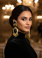 Gold and black decorative earrings on a textured white surface