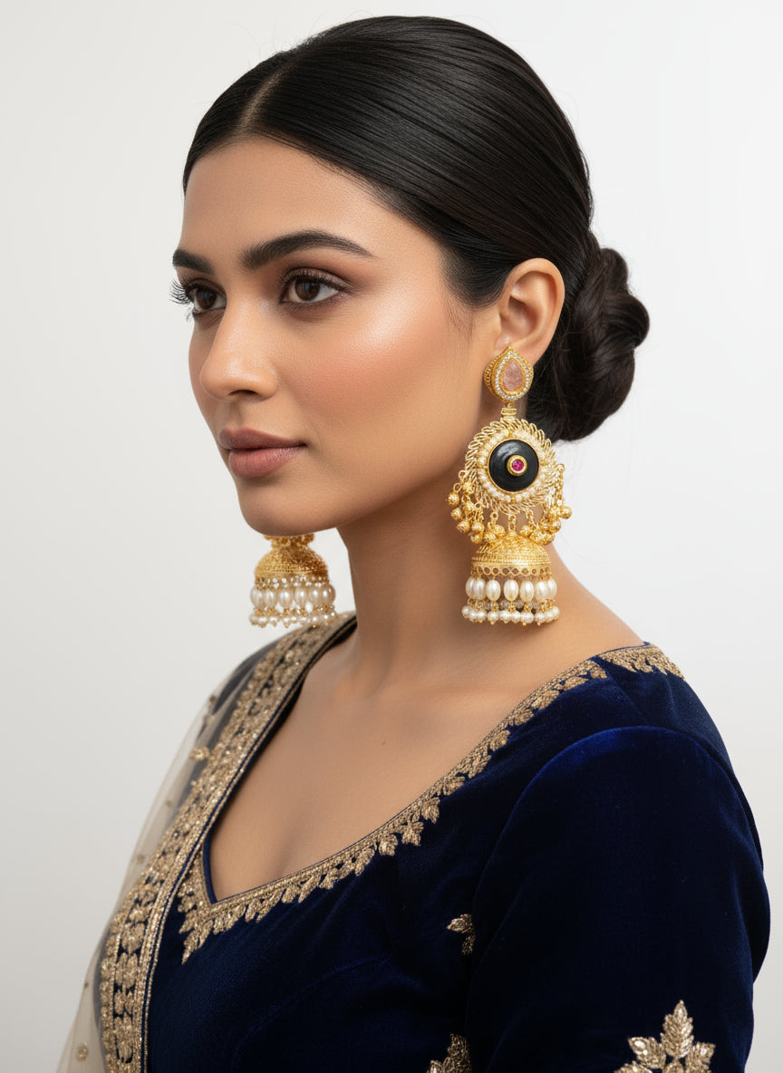 Gold and black earrings with gemstones held in a hand, with a blurred background of more jewellery.
