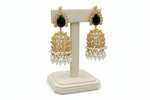 Gold and black earrings with pearl drops on a white stand against a pure white background