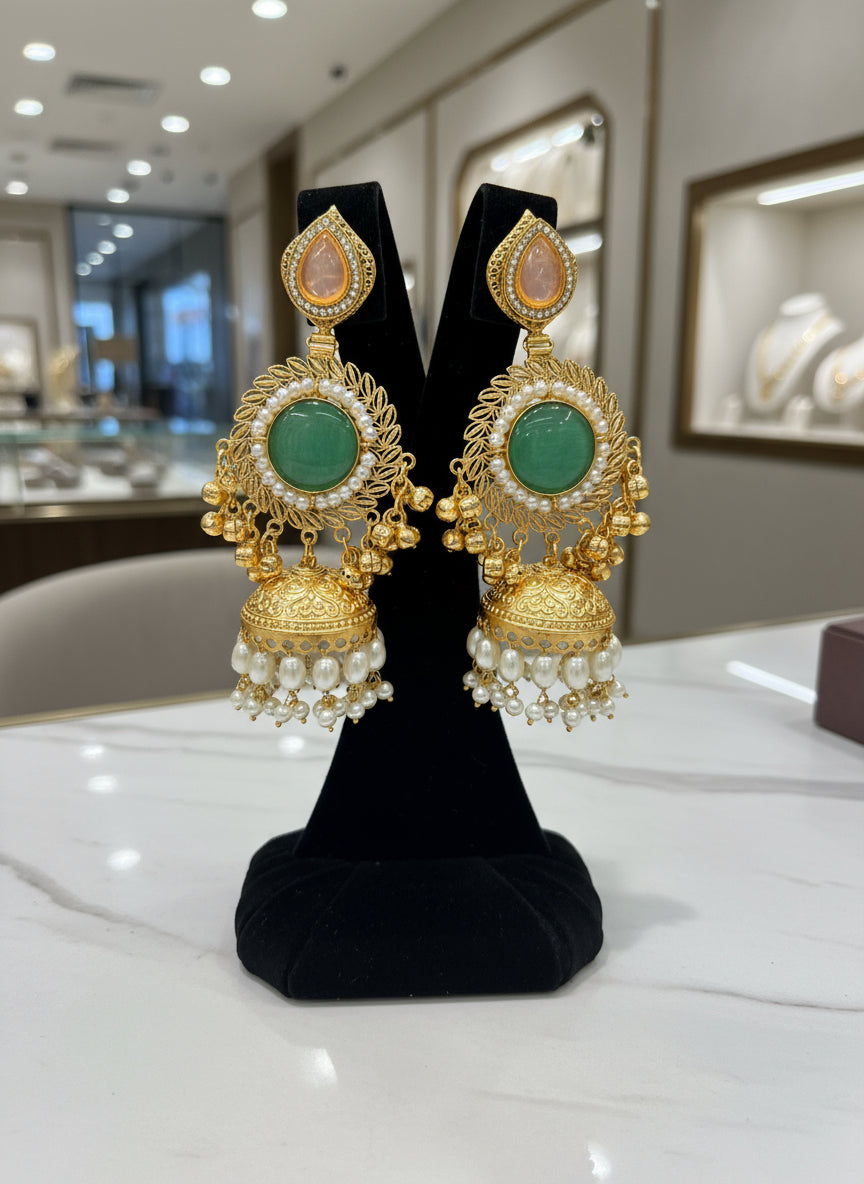 Gold and green gemstone earrings held by a hand with a blurred jewellery store background.