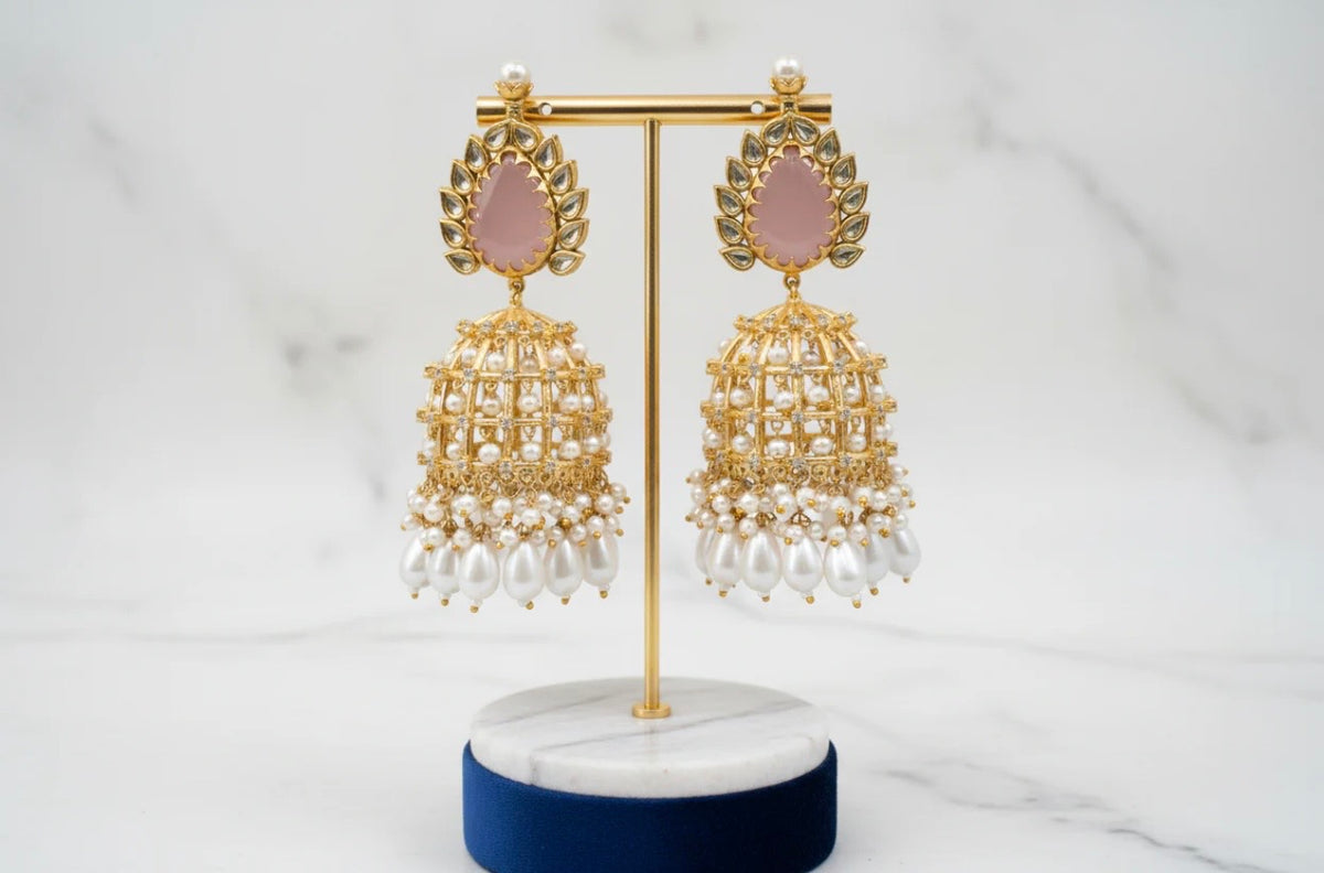 Gold and pearl earrings on a white stand with a white background