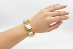 Gold bracelet with large mother of pearl stones on a wrist against a white background