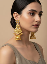 A pair of gold-plated long Jhumka earrings with intricate traditional design and miniature bells, displayed on a stand.