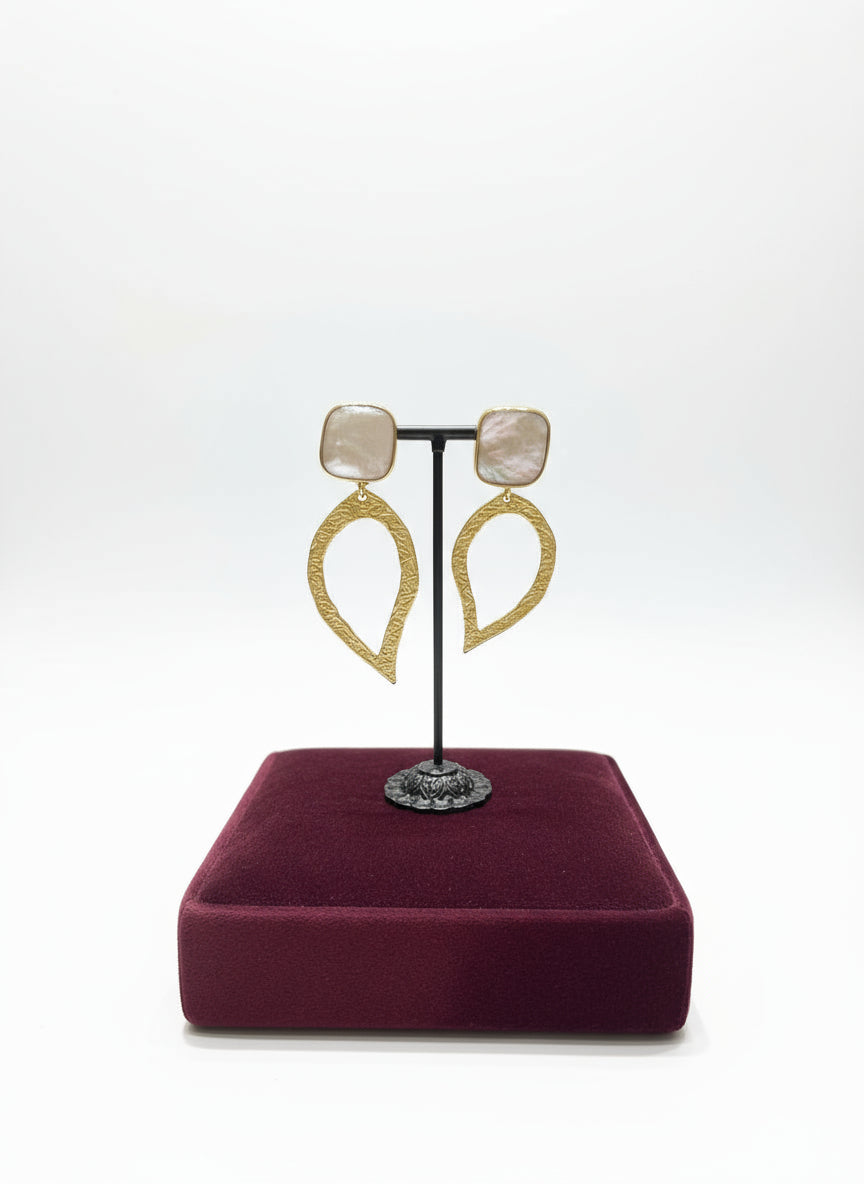 Gold earrings on a stand with a burgundy cushion in a jewelry store setting