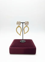Gold earrings on a stand with a burgundy cushion in a jewelry store setting