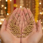 Gold earrings with beads held in hands against a festive background