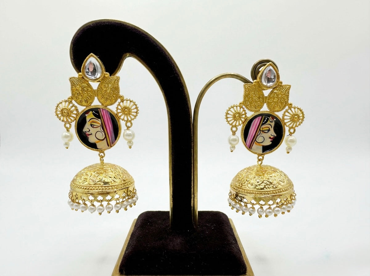 Gold earrings with face design on a black stand against a white background