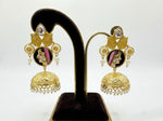Gold earrings with face design on a black stand against a white background