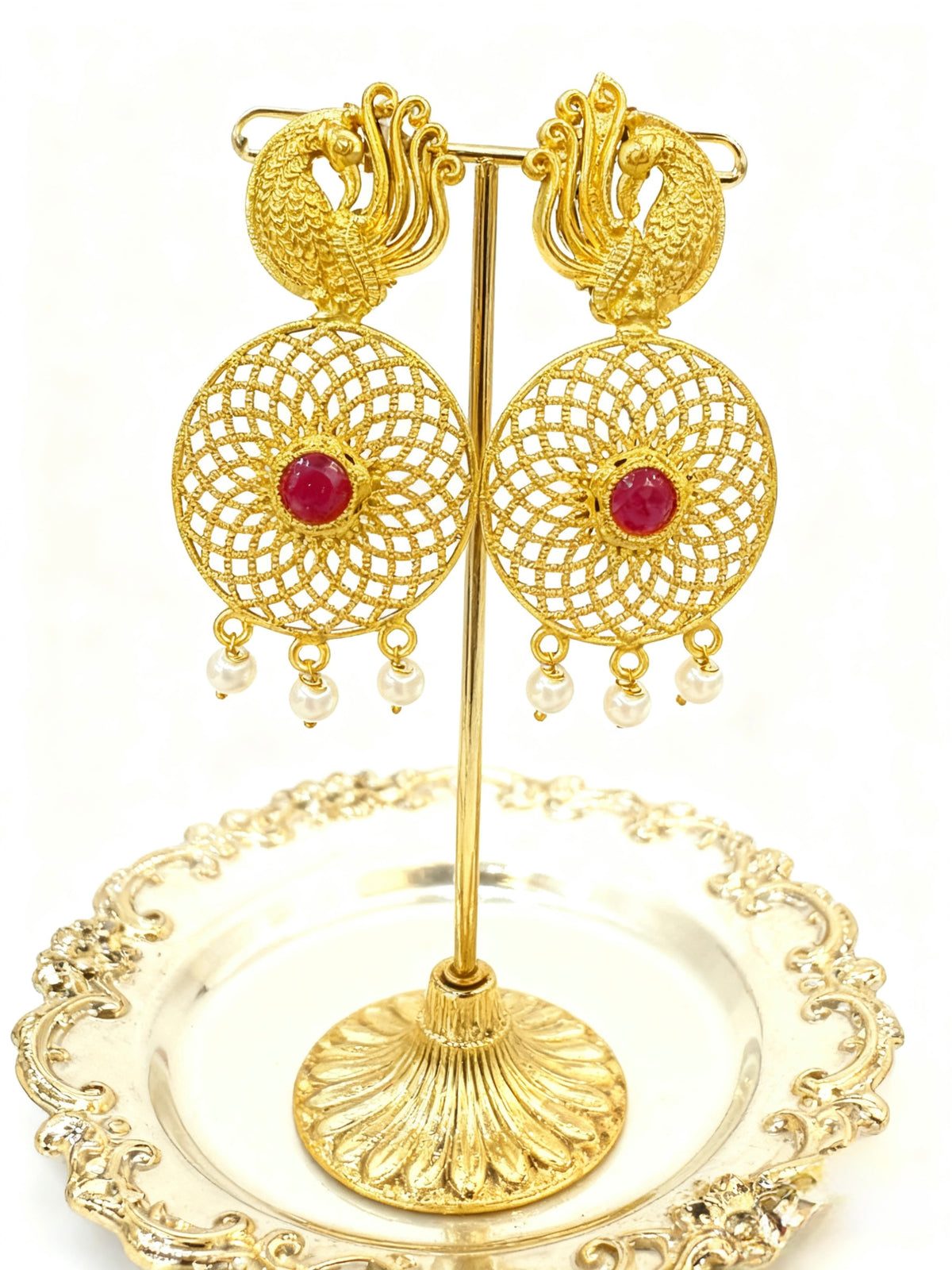 Gold earrings with red gemstones on a decorative stand
