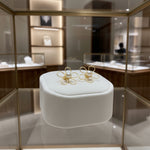 Gold flower-shaped earrings on a white cushion in a jewelry store setting