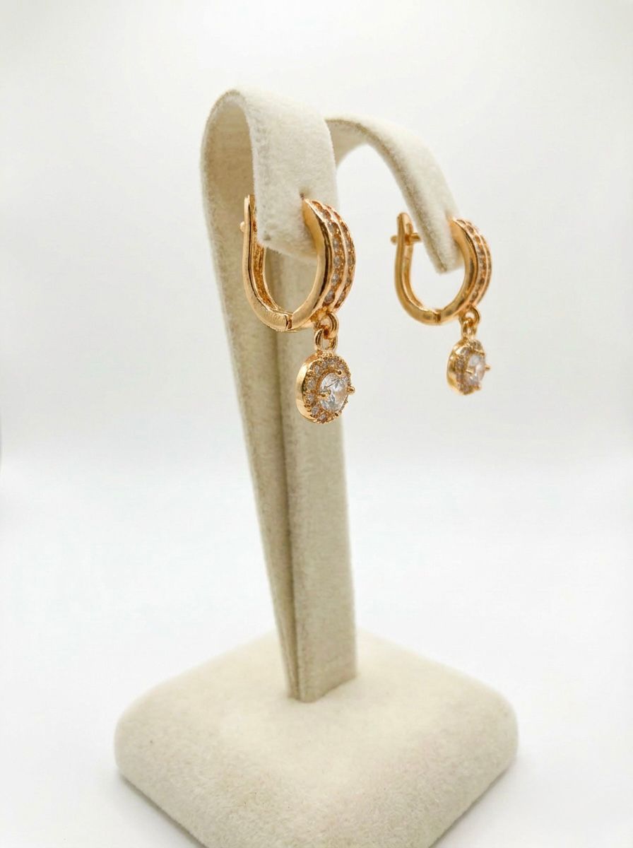 Gold hoop earrings with gemstones on a beige stand against a white background