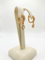 Gold hoop earrings with gemstones on a beige stand against a white background
