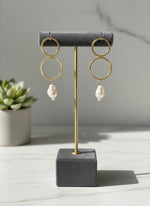 Gold hoop earrings with pearls on a grey stand against a neutral background