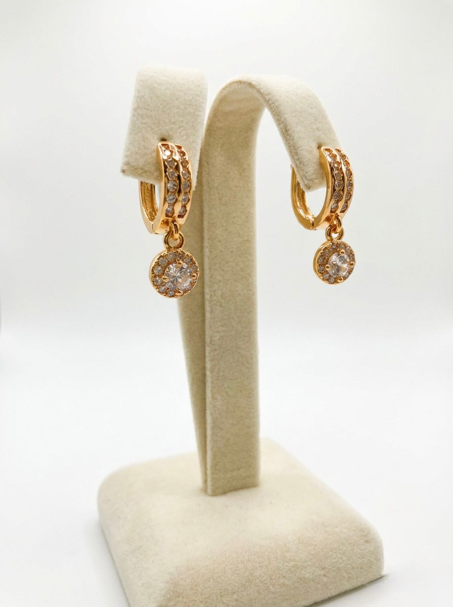 Gold hoop earrings with round embellishments on a beige earring stand against a white background