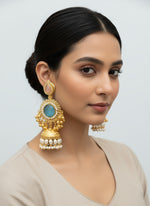 Gold and turquoise earrings held by a hand with a blurred background