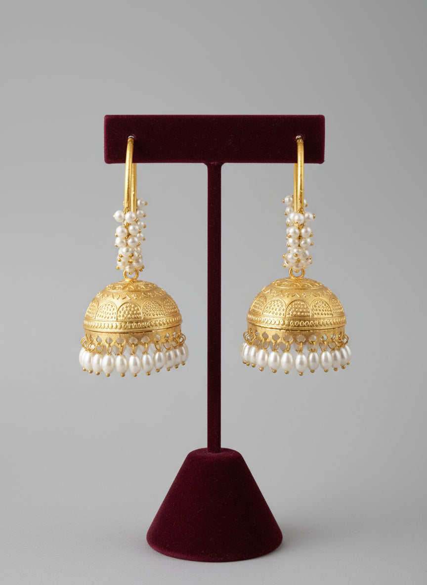 Gold hoop earrings with intricate designs on a stand against a textured white background