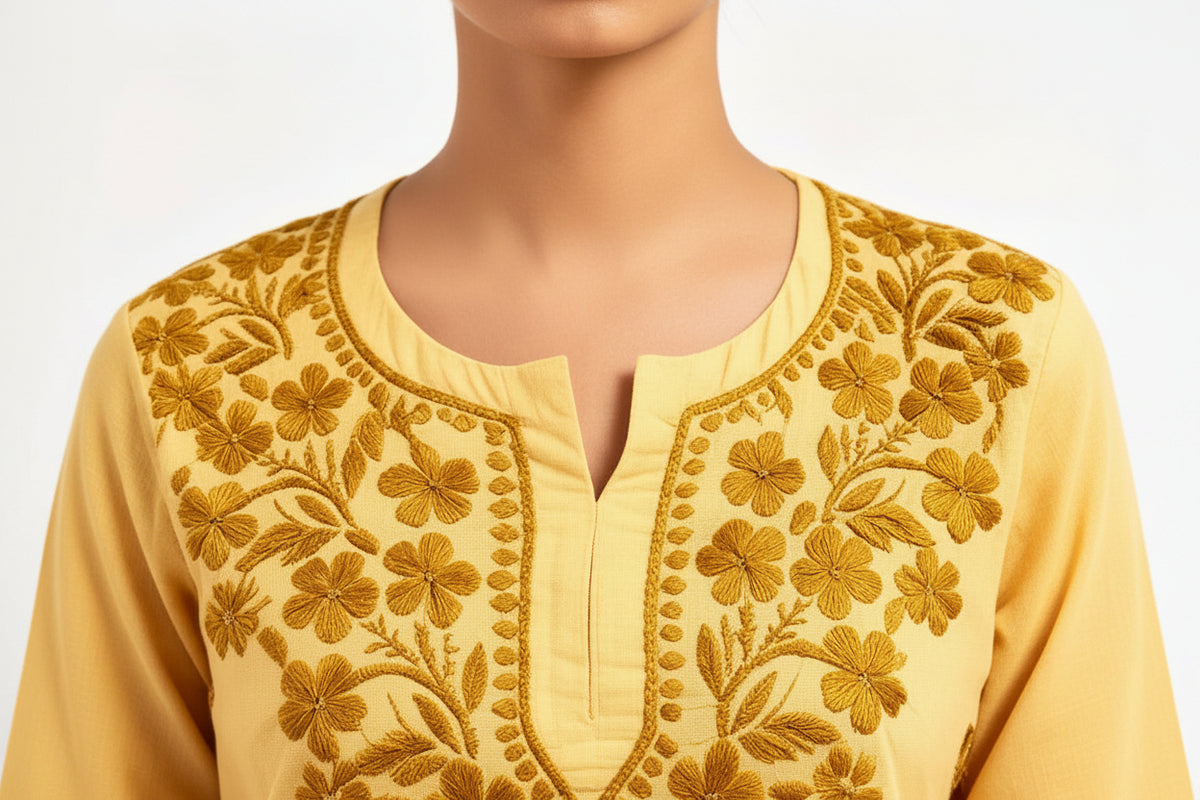 A close-up view of a person wearing a yellow embroidered short kurti with detailed floral embroidery along the split round neckline.