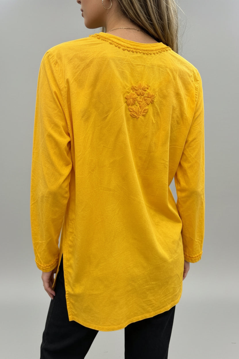 Rear view of a woman wearing a vibrant yellow cotton short kurti featuring a delicate floral motif embroidered on the back yoke and a square hem line, paired with dark trousers in an indoor boutique setting.