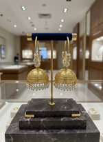 Gold earrings with intricate designs on a stand against a textured white background