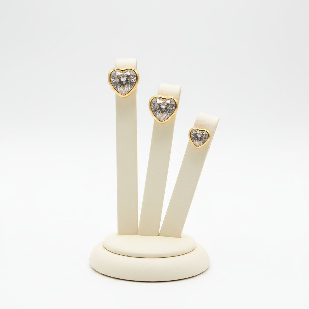 Golden heart-shaped stud earrings in graduated sizes, each featuring a central crystal on a stand. 