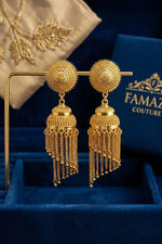 A pair of gold-plated jhumka earrings with ornate circular floral studs and dangling multi-layered chain fringes, branded as Famaza Couture .