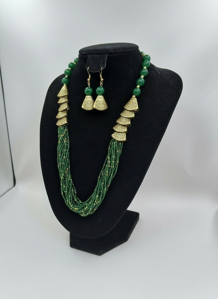 Green beaded necklace with gold accents and matching earrings on a posh jewellery dummy.