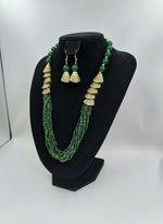 Green beaded necklace with gold accents and matching earrings on a posh jewellery dummy.