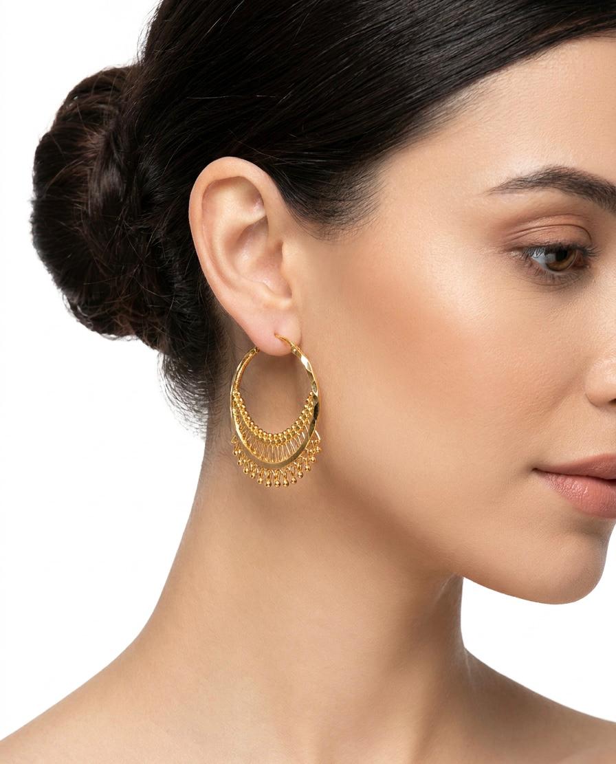 A posh model wearing luxury gold-plated hoop earrings featuring a crescent chandbali design with intricate beaded filigree drops for Famaza Couture.