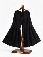 Front view of a black cotton tiered gharara featuring intricate antique silver Kaamdani and Bakhiya threadwork, displayed on a wooden stand.