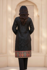 Back view of a woman wearing a black silk kurta set with detailed Kanni embroidery on the hem and a matching embellished dupatta.