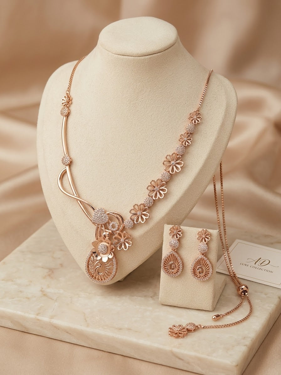 Rose gold jewelry set displayed on a cream jewelry bust, including a necklace with floral motifs, matching earrings, and a chain with a small box, set against a warm beige satin background.