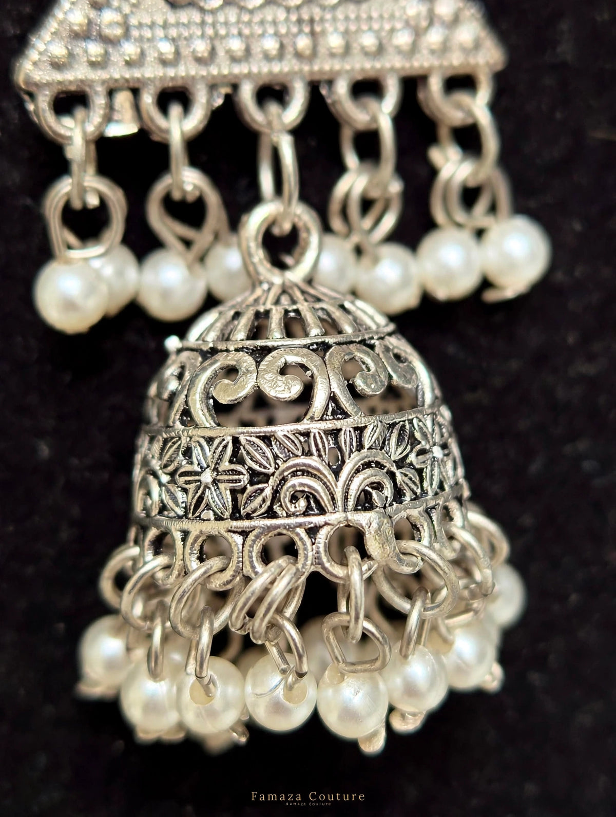 Silver-toned traditional Indian jhumka earrings with intricate filigree detailing and dangling white pearl beads, shown against a black background.