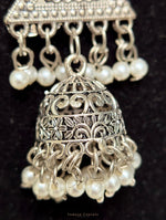 Silver-toned traditional Indian jhumka earrings with intricate filigree detailing and dangling white pearl beads, shown against a black background.