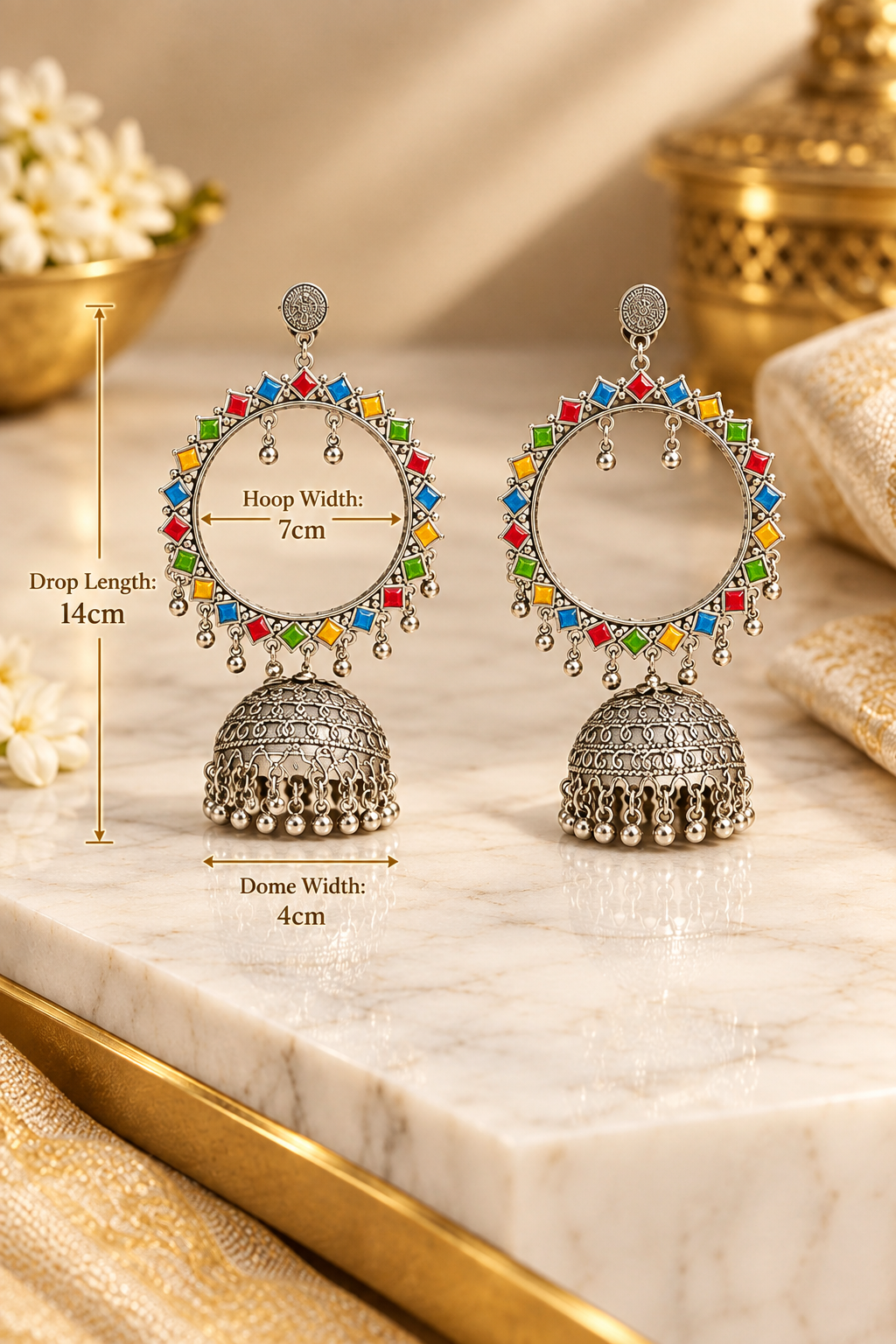 A pair of silver-toned Indian jhumka earrings with multicolor gemstone accents, displayed on a white marble surface with dimension overlays showing measurements.