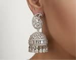 A close-up of a model's ear wearing a highly detailed silver-toned Indian jhumka earring adorned with clear stones.