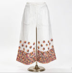 Wide-leg white pants on a mannequin, featuring intricate multi-color floral embroidery at the hem and scattered motifs above. Against a plain white background.
