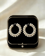Pair of hand-woven ivory pearl cluster hoop earrings with gold-tone accents, displayed on black velvet jewelry box — Famaza Couture bridal luxury.