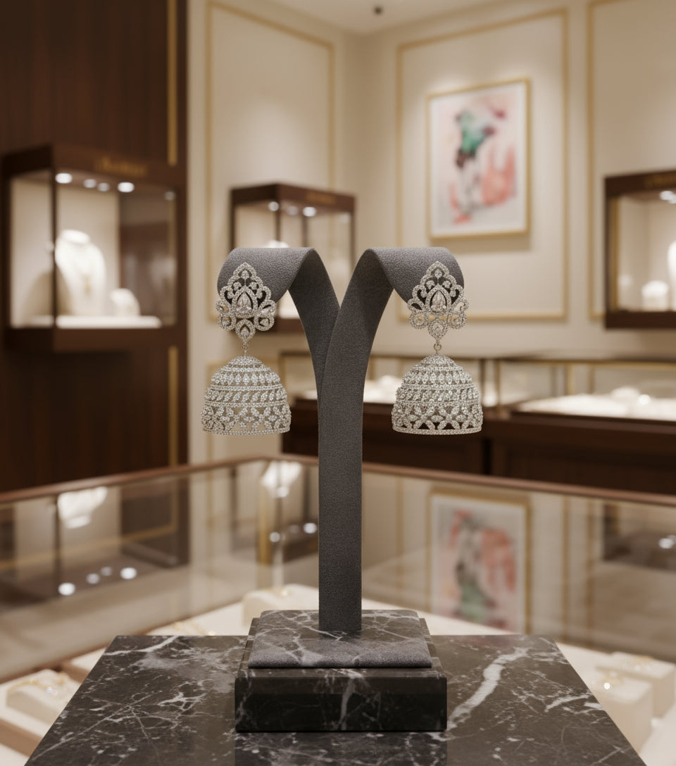 A pair of silver finish, American diamond jumbo jhumka earrings displayed on a stand against a black background.